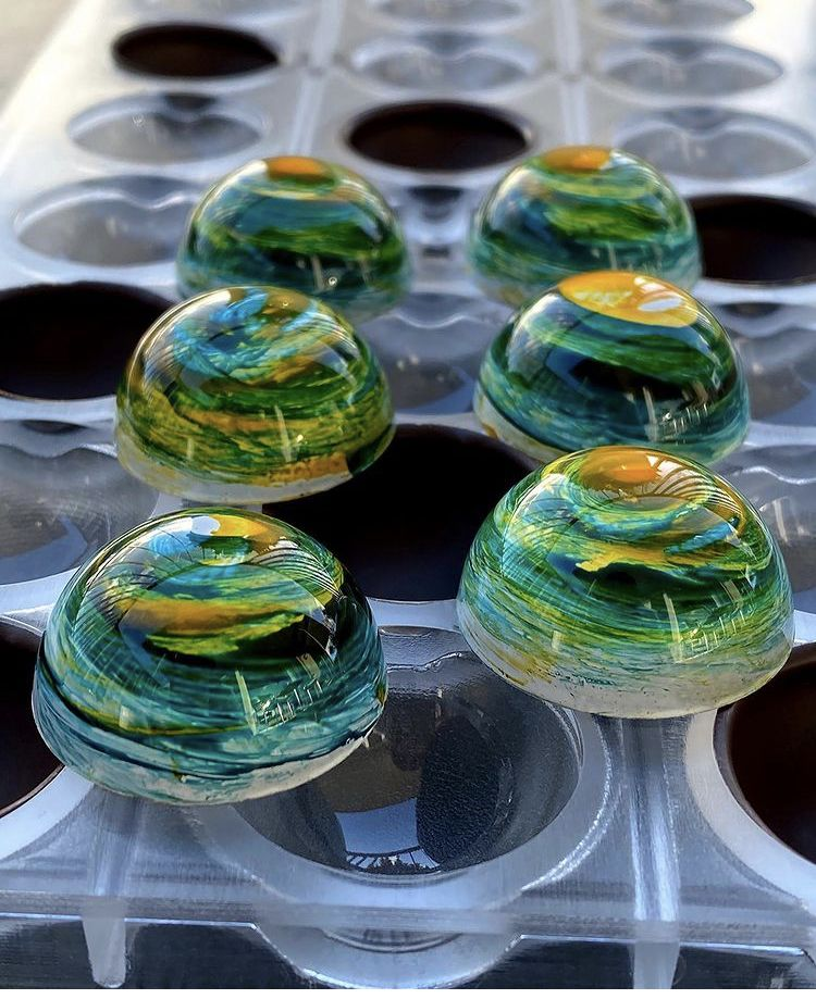 Glossy green and gold dome-shaped chocolate bonbons resting in a clear mold.